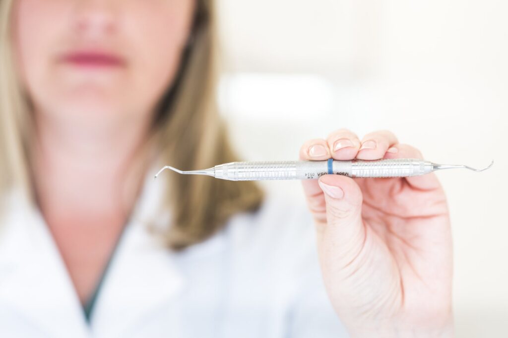 A dentist holding a thin dental explorer in a gloved hand